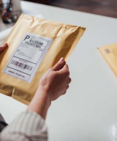 Hands of an unrecognisable small business owner holding a yellow envelope with shipping details before dispatching it