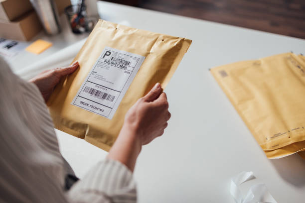 Hands of an unrecognisable small business owner holding a yellow envelope with shipping details before dispatching it